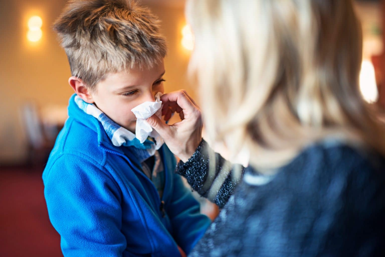 Pediatric-Allergy-symptoms A young boy experiencing allergies blows his nose into a tissue.