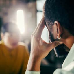Mid-adult man holds his hand to his forehead in a close, thoughtful moment, conveying stress, headache and trouble hearing in conversation
