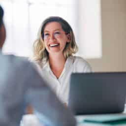 A cheerful woman with glasses is sitting at a desk, engaged in a friendly doctor appointment.
